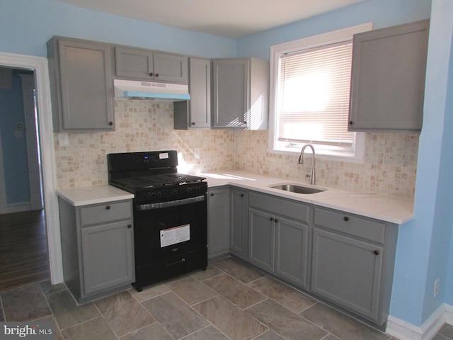 kitchen with gray cabinets, backsplash, black gas stove, a sink, and under cabinet range hood