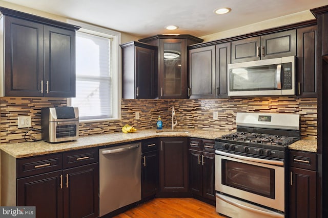 kitchen featuring dark brown cabinetry, sink, light stone counters, light hardwood / wood-style flooring, and appliances with stainless steel finishes