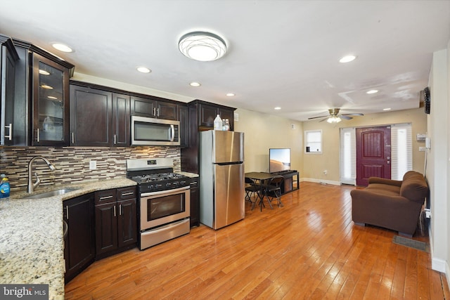 kitchen with sink, light hardwood / wood-style flooring, light stone countertops, appliances with stainless steel finishes, and dark brown cabinets