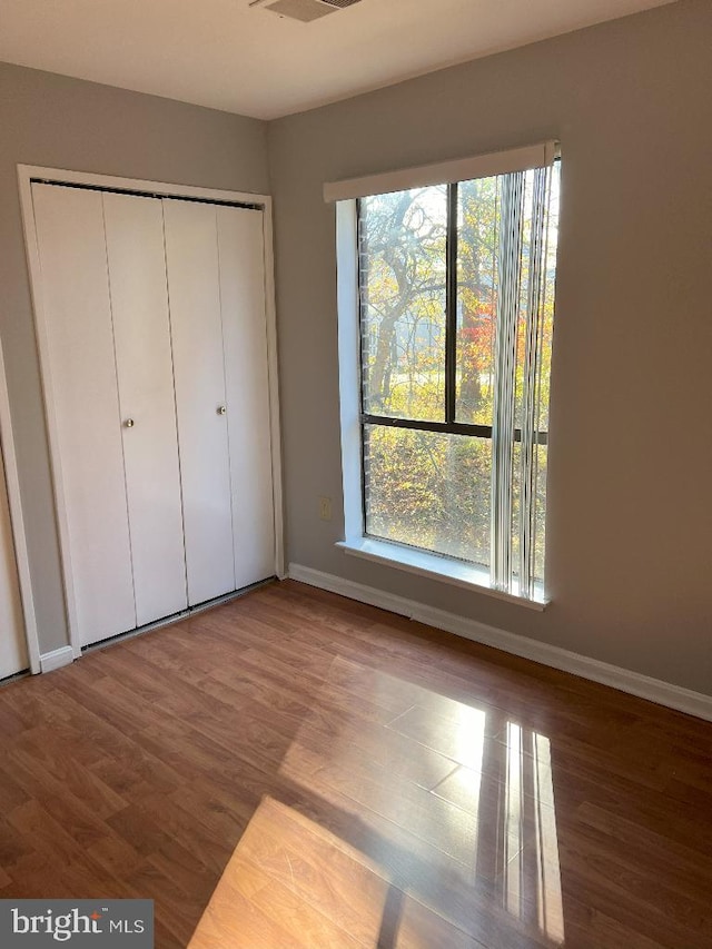 unfurnished bedroom with multiple windows, a closet, and hardwood / wood-style floors