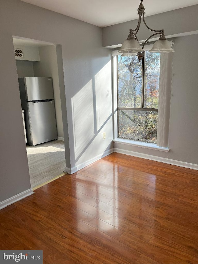 unfurnished dining area featuring hardwood / wood-style flooring and an inviting chandelier