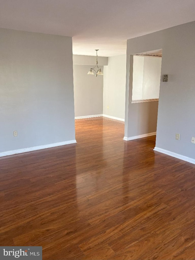 empty room featuring an inviting chandelier and dark wood-type flooring