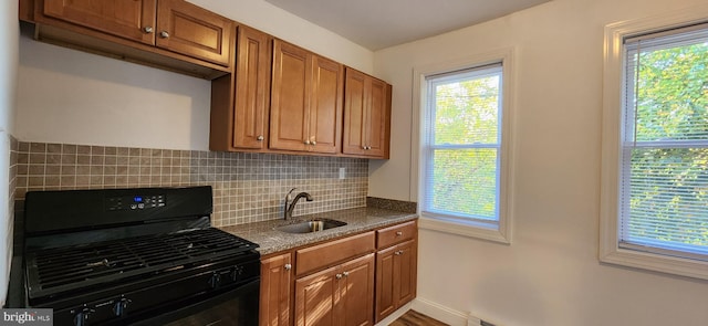 kitchen featuring dark stone counters, sink, hardwood / wood-style flooring, black gas range oven, and tasteful backsplash