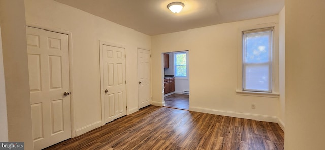 unfurnished bedroom featuring dark hardwood / wood-style flooring, baseboard heating, and multiple closets