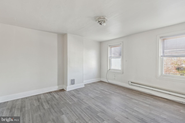 spare room featuring baseboard heating, a healthy amount of sunlight, and light hardwood / wood-style floors