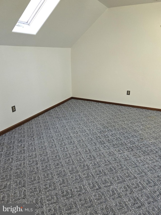 additional living space with lofted ceiling with skylight and dark colored carpet