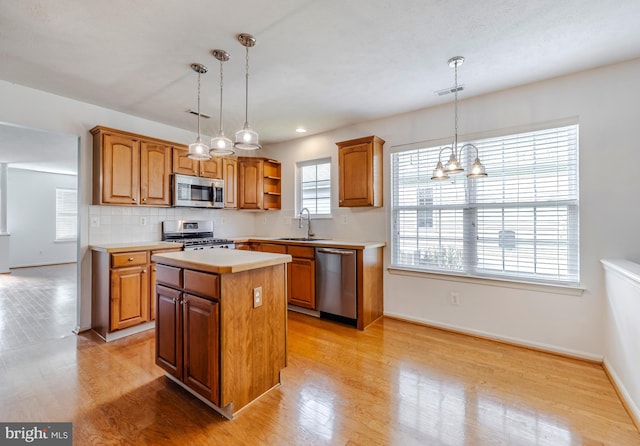 kitchen with appliances with stainless steel finishes, decorative light fixtures, a chandelier, light hardwood / wood-style floors, and a kitchen island