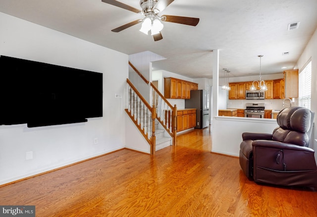 living room featuring ceiling fan with notable chandelier and light wood-type flooring