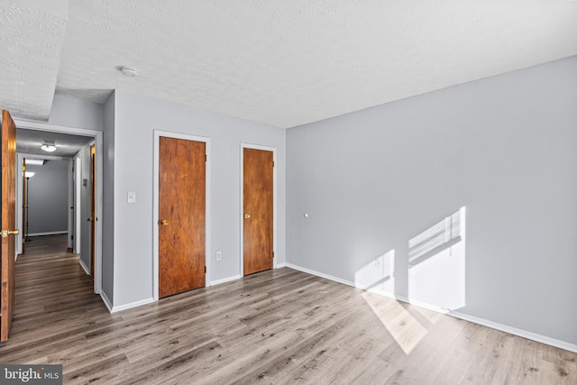 unfurnished bedroom with a textured ceiling, two closets, and light wood-type flooring