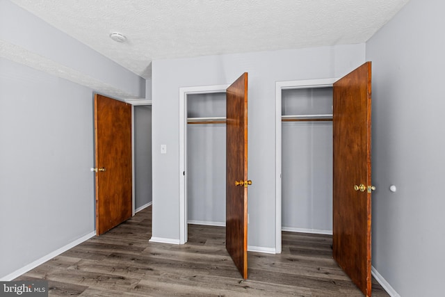 unfurnished bedroom with a textured ceiling, dark hardwood / wood-style flooring, and two closets