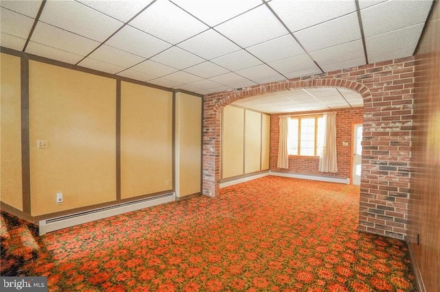 unfurnished living room with baseboard heating, a paneled ceiling, carpet floors, and brick wall