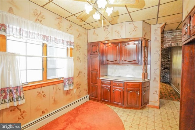 kitchen with a paneled ceiling, ceiling fan, brick wall, and a baseboard heating unit