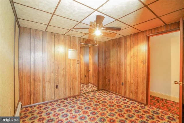 basement with a paneled ceiling, ceiling fan, and wooden walls