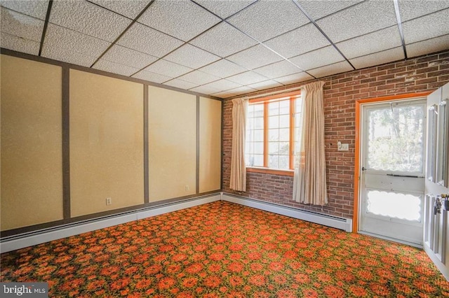 spare room with a paneled ceiling, carpet floors, and brick wall