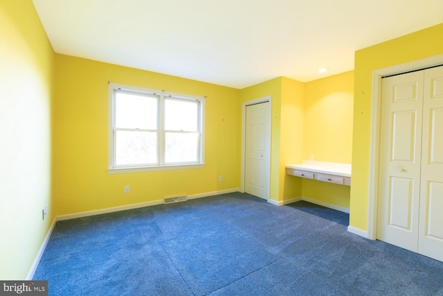 unfurnished bedroom featuring dark carpet and multiple closets