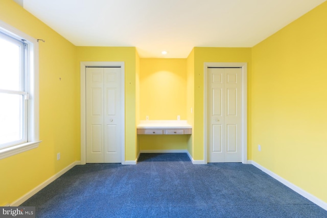 unfurnished bedroom featuring two closets and dark colored carpet