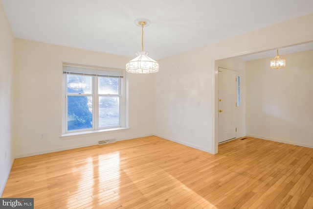 empty room featuring light wood-type flooring and an inviting chandelier