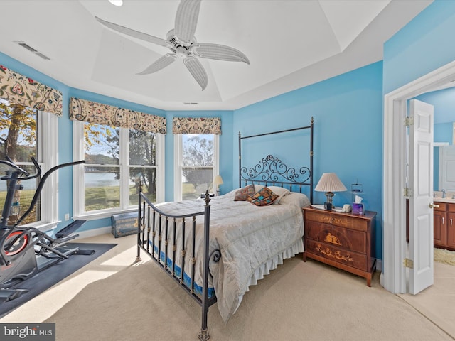 carpeted bedroom with a raised ceiling, connected bathroom, ceiling fan, and sink