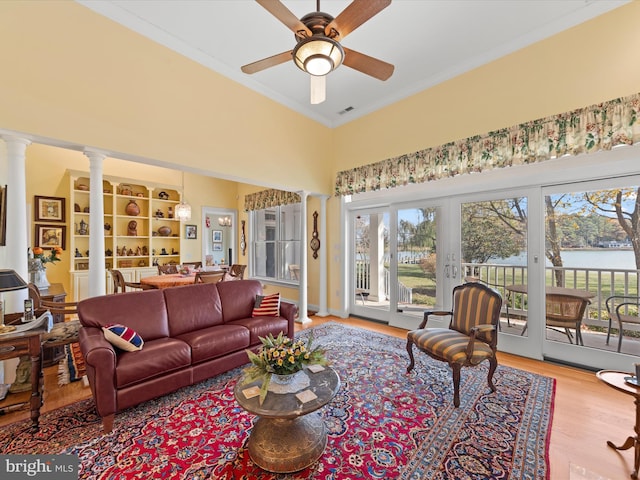 living room featuring a water view, crown molding, ceiling fan, light wood-type flooring, and ornate columns