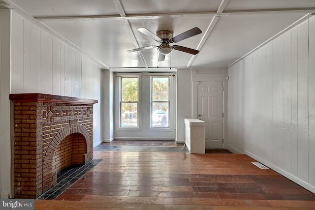 unfurnished living room with ceiling fan, wood walls, dark hardwood / wood-style floors, and a brick fireplace