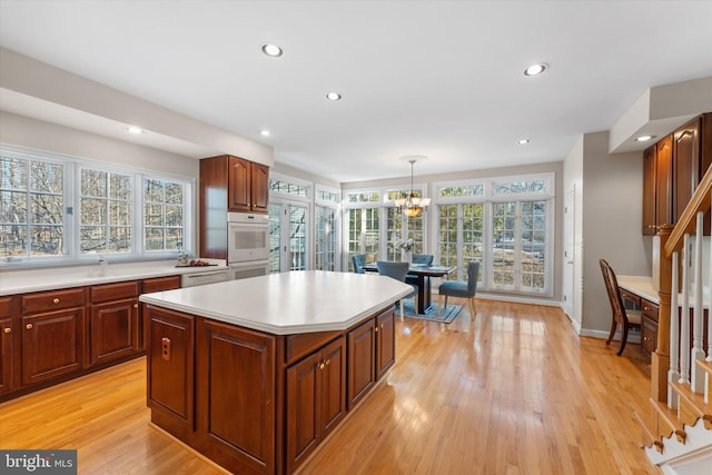 kitchen with decorative light fixtures, white double oven, a center island, a notable chandelier, and light hardwood / wood-style flooring