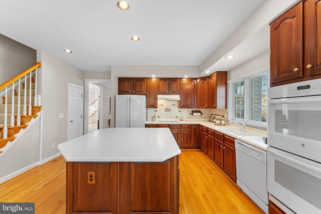 kitchen featuring sink, a kitchen island, white appliances, light hardwood / wood-style floors, and backsplash