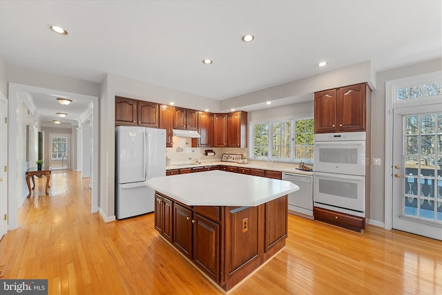 kitchen with white appliances, light hardwood / wood-style flooring, a center island, and a healthy amount of sunlight