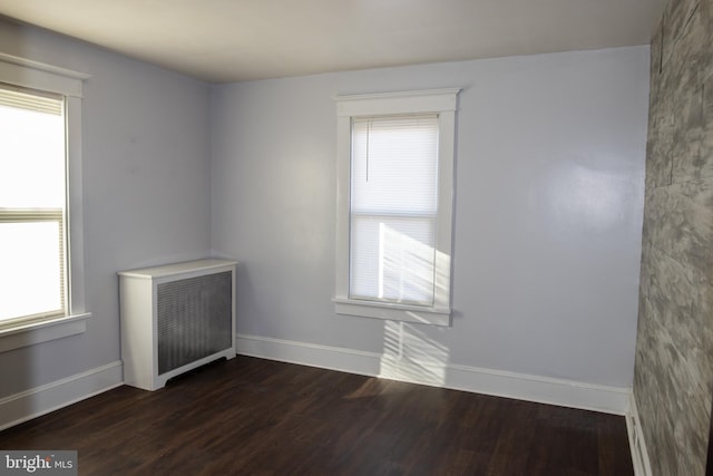 unfurnished room with radiator heating unit and dark hardwood / wood-style floors