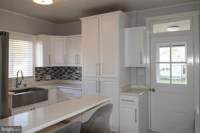 kitchen featuring plenty of natural light, crown molding, white cabinetry, and sink