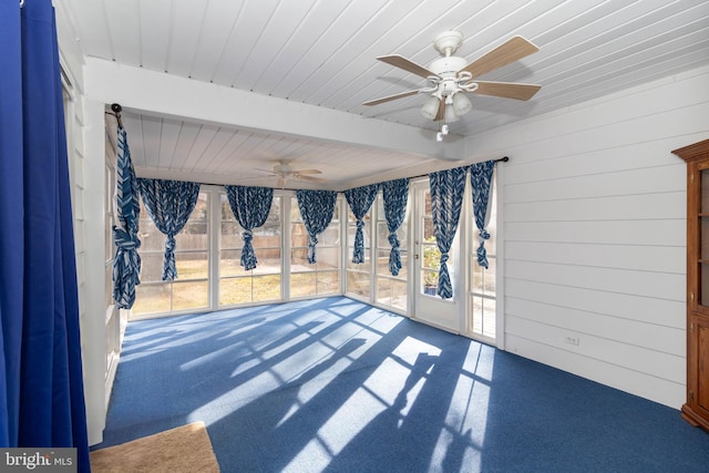 spare room with carpet flooring, wood walls, beamed ceiling, and ceiling fan