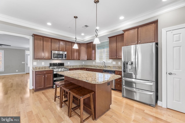 kitchen featuring a center island, light hardwood / wood-style floors, decorative light fixtures, appliances with stainless steel finishes, and ornamental molding