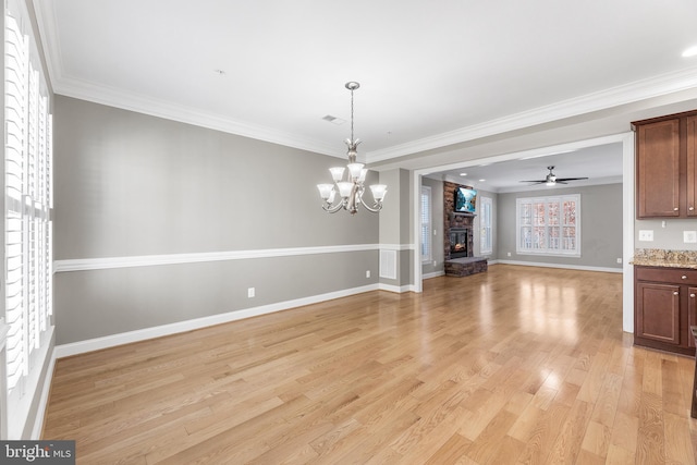 interior space featuring light wood-type flooring, ceiling fan with notable chandelier, crown molding, a stone fireplace, and plenty of natural light