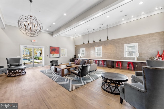 living room with ornamental molding, a towering ceiling, beam ceiling, light hardwood / wood-style floors, and a chandelier