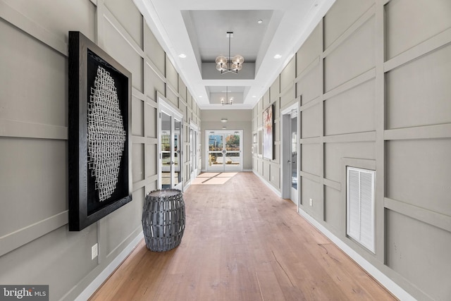 corridor featuring french doors, light hardwood / wood-style flooring, a raised ceiling, and a notable chandelier