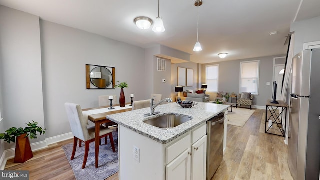 kitchen with appliances with stainless steel finishes, light wood-type flooring, sink, pendant lighting, and white cabinets