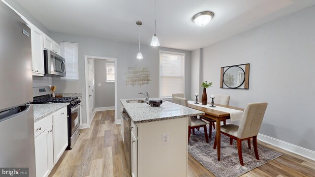 kitchen featuring appliances with stainless steel finishes, light wood-type flooring, decorative light fixtures, and a kitchen island with sink