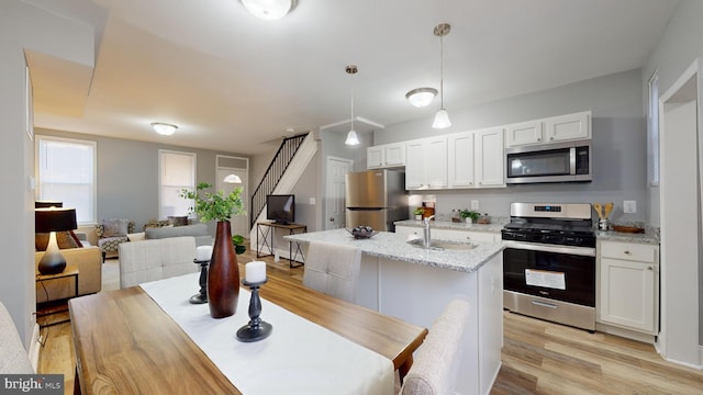 kitchen featuring hanging light fixtures, appliances with stainless steel finishes, light hardwood / wood-style floors, light stone counters, and white cabinetry