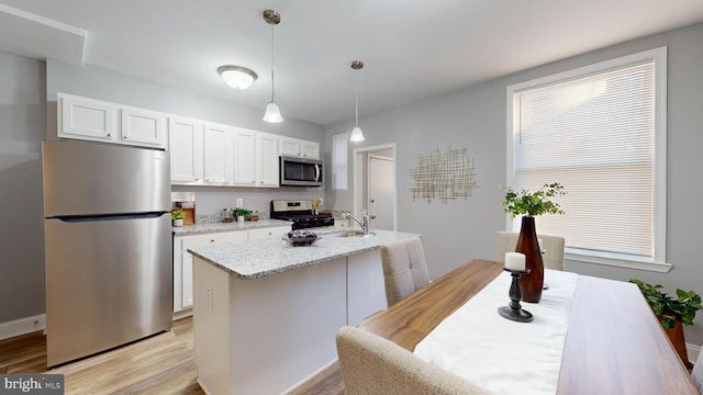 kitchen with white cabinetry, stainless steel appliances, pendant lighting, a kitchen island with sink, and light wood-type flooring