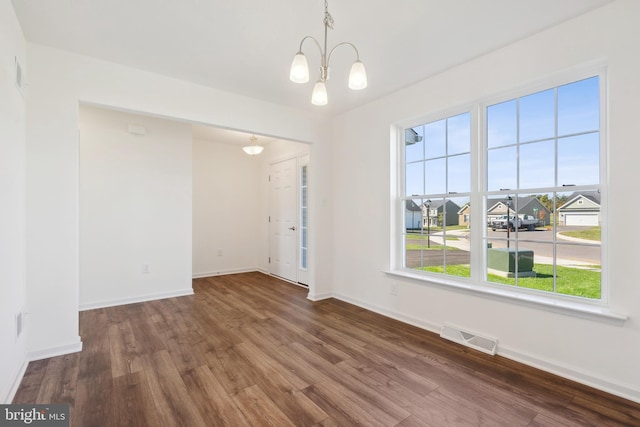 unfurnished room featuring a notable chandelier, plenty of natural light, and dark wood-type flooring