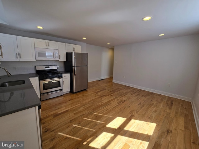 kitchen with sink, backsplash, light hardwood / wood-style floors, white cabinets, and appliances with stainless steel finishes