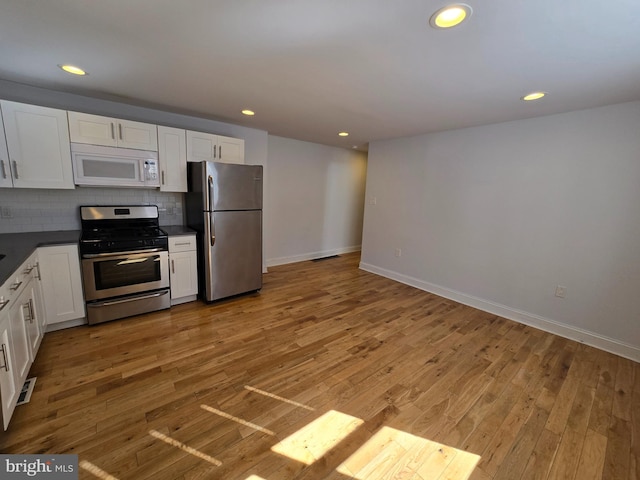 kitchen featuring white cabinets, wood-type flooring, backsplash, and stainless steel appliances