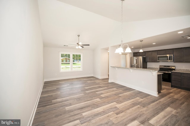 kitchen featuring light stone countertops, appliances with stainless steel finishes, a kitchen breakfast bar, dark brown cabinetry, and wood-type flooring