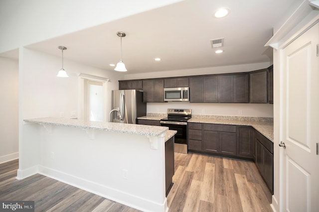 kitchen featuring decorative light fixtures, light stone countertops, light wood-type flooring, dark brown cabinets, and stainless steel appliances