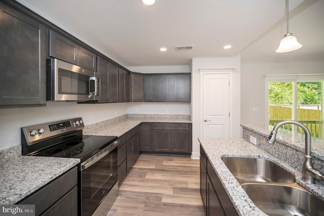 kitchen with light stone countertops, appliances with stainless steel finishes, dark brown cabinets, sink, and light hardwood / wood-style floors