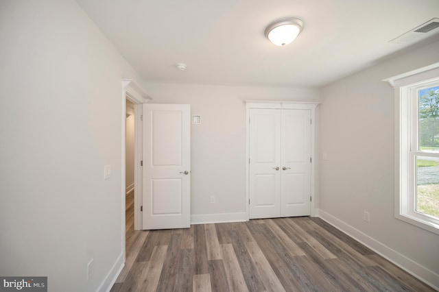 unfurnished bedroom featuring multiple windows, a closet, and hardwood / wood-style flooring