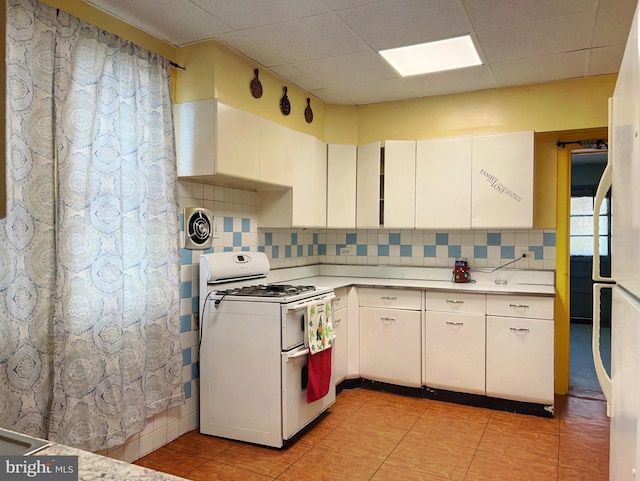 kitchen featuring white cabinetry, backsplash, light tile patterned floors, and gas range gas stove