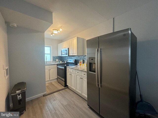 kitchen featuring light wood-type flooring, backsplash, stainless steel appliances, sink, and white cabinetry