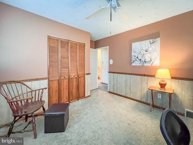 living area featuring ceiling fan, light colored carpet, and wooden walls