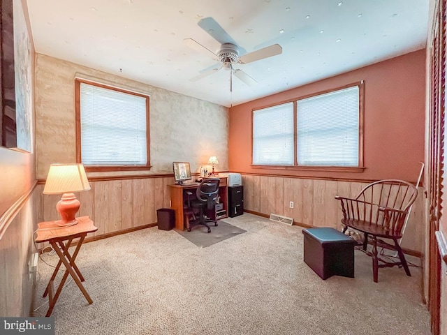 office area with light colored carpet, ceiling fan, and wood walls