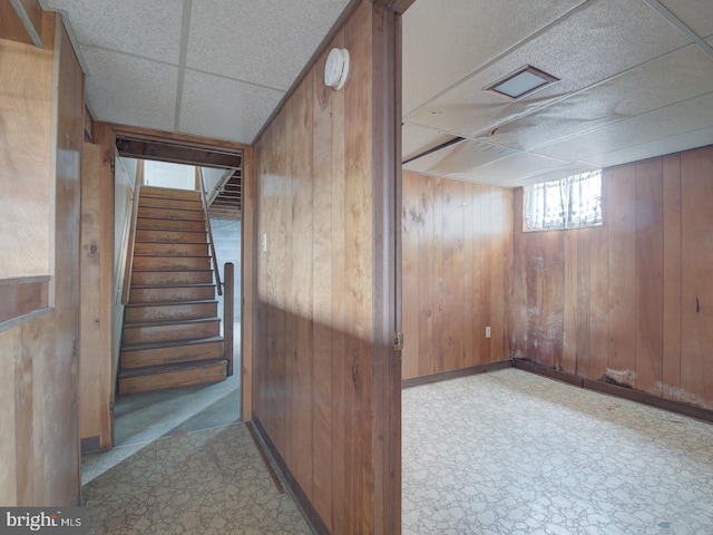 basement featuring a drop ceiling and wooden walls